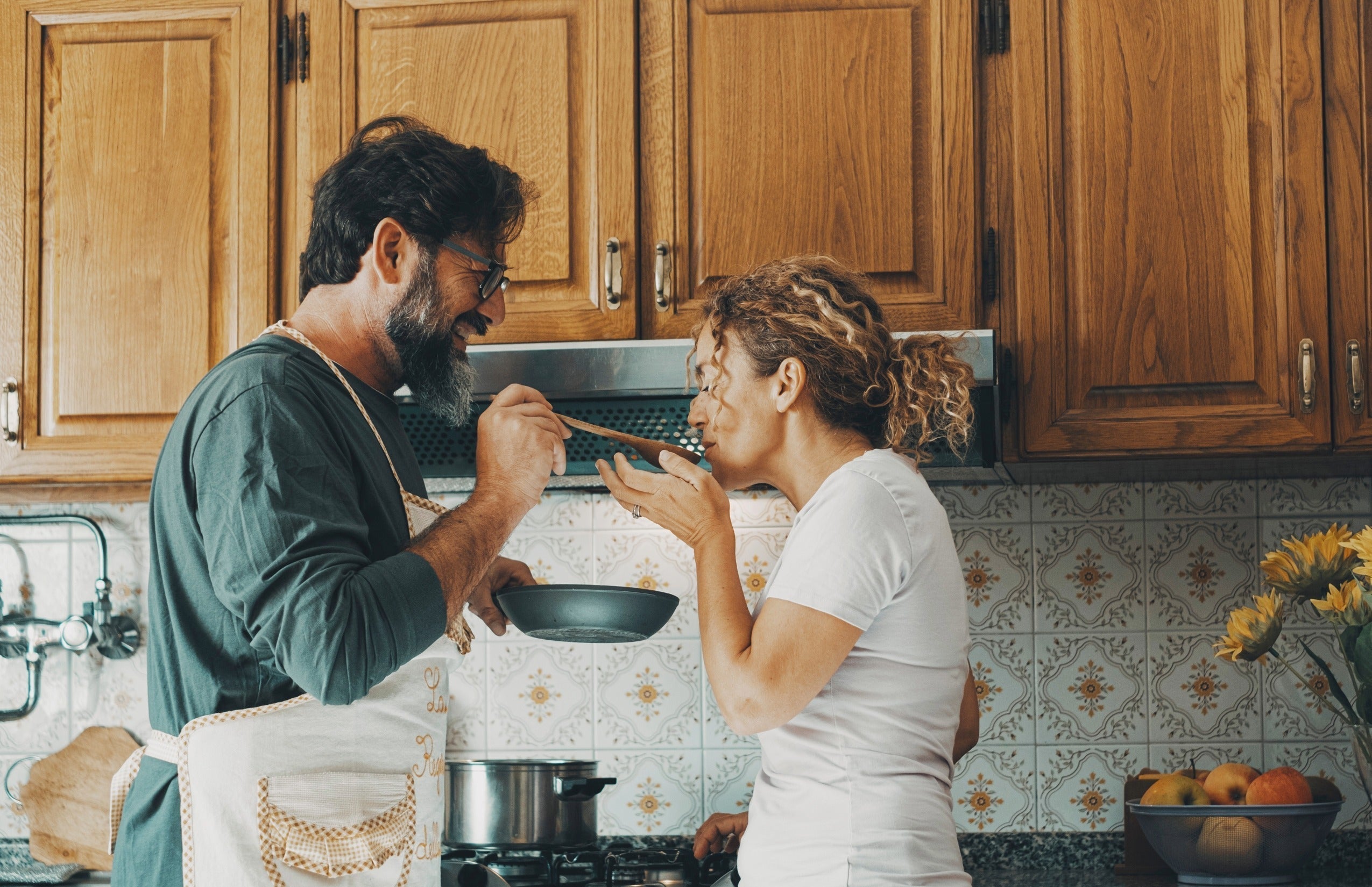 A couple cooking and tasting food together at home.