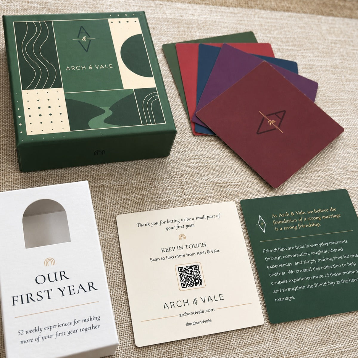 Arch & Vale first-year marriage card set displayed on a textured beige fabric background, including a green gift box, four colored cards, a white 'Our First Year' card, and a green instruction card.