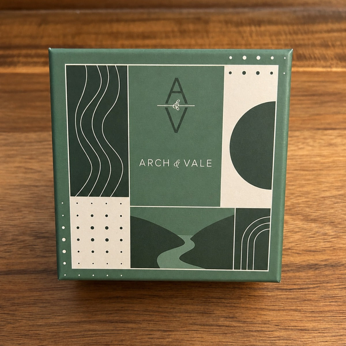 A square green product box with abstract geometric panel designs and the text 'ARCH & VALE' on the front, photographed on a wooden tabletop.